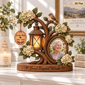 May include: A memorial tabletop sculpture featuring a brown tree branch frame with a lantern, a robin, and hydrangea flowers. It includes an oval photo frame, a hanging wooden disc inscribed with Evelyn Rose 1946-2024, and a base with the text Loved Beyond Words.