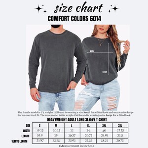 May include: A size chart for the Comfort Colors 6014 heavyweight adult long sleeve t-shirt. The image displays a dark grey long sleeve t-shirt on two models, with a table listing width, length, and sleeve length measurements in inches for sizes S to 3XL.