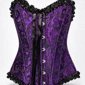 May include: A purple and black corset featuring a damask pattern, a sweetheart neckline, and black ruffled trim along the top and bottom edges. The front includes a vertical row of silver-toned metal busk closures and long black satin ribbon ties.