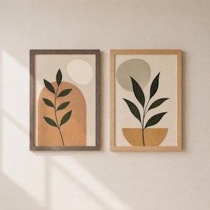 May include: Two framed wall art prints featuring botanical illustrations. The left print shows a dark green leafy branch over a terracotta arch and cream circle. The right print displays a dark green plant in a gold bowl under a sage green circle.