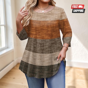 May include: A three-quarter sleeve tunic top featuring a horizontal color-blocked pattern in shades of beige, burnt orange, dark brown, and gray. The garment has a round neckline and a flared hemline, paired with blue denim jeans.