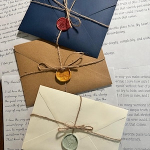 May include: Three envelopes in navy blue, kraft brown, and cream, each tied with thin jute twine and secured with a wax seal. The navy envelope has a red seal, the brown envelope has a gold seal, and the cream envelope has a pale green seal.