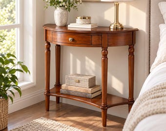 May include: A semi-circular wooden console table with a warm brown finish, featuring a single central drawer with a small round knob, four turned legs, and a lower storage shelf. The table surface holds a lamp, a vase, and a small box.