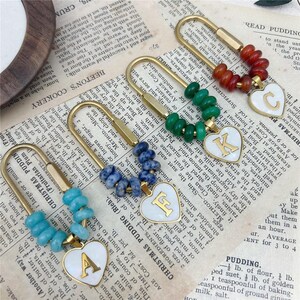 Peut inclure: Quatre épingles à nourrice en métal doré, chacune ornée d'une rangée de petites perles rondes turquoise, bleues, vertes et brun rougeâtre. Chaque épingle comporte un pendentif en forme de cœur blanc avec une lettre A, F, K ou C dorée.