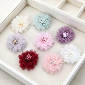 Può includere: Otto decorazioni floreali in tessuto a strati di vari colori, tra cui bianco, azzurro, lavanda, rosa, viola, bordeaux e rosa pallido. Ogni fiore presenta un centro composto da piccole perline e petali delicati e arricciati.