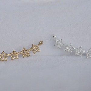 May include: Two delicate, curved jewelry pieces made of metal. One is gold and the other is silver. Each piece is made up of a series of small, star-shaped links.