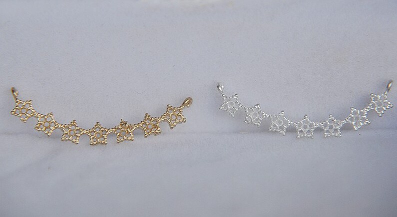 May include: Two delicate, curved jewelry pieces made of metal. One is gold and the other is silver. Each piece is made up of a series of small, star-shaped links.