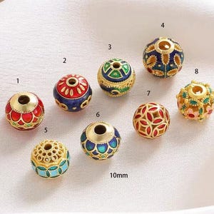 Peut inclure: Dix perles rondes de 10 mm avec des motifs complexes et de l'émail coloré. Les perles sont dorées et présentent une variété de motifs, notamment des motifs floraux, géométriques et abstraits. Les perles sont parfaites pour la fabrication de bijoux, l'artisanat et la décoration intérieure.