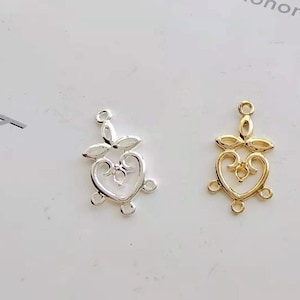 May include: Two ornate metal heart-shaped charms, one silver and one gold, with intricate details and a loop at the top for attaching to jewellery or other crafts.