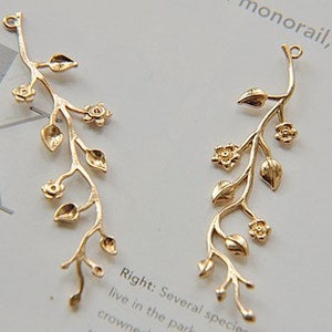 May include: Two gold-tone metal charms shaped like a vine with leaves and flowers. The charms have a loop at the top for attaching to jewellery or other crafts.