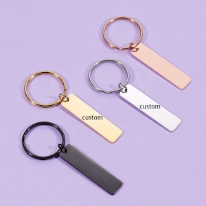 Peut inclure: Quatre porte-clés avec une étiquette rectangulaire indiquant "custom". Les porte-clés sont dorés, argentés, or rose et noirs.