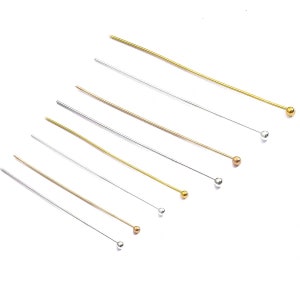 May include: Assortment of gold and silver head pins with round ball heads. The pins are arranged in order of size, with the smallest pin at the top and the largest pin at the bottom.