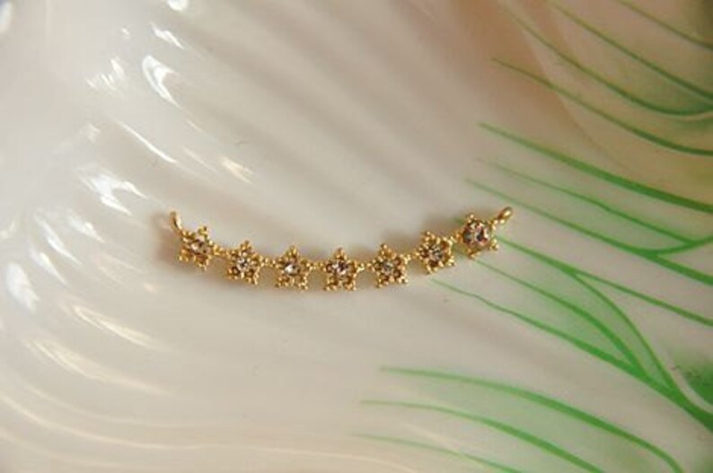 May include: Gold-toned star-shaped charm with clear rhinestones. The charm is designed to be used as a jewelry component.