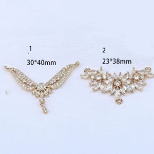 May include: Two gold-tone pendant connectors with clear crystal embellishments. The connector on the left measures 30mm by 40mm. The connector on the right measures 23mm by 38mm.