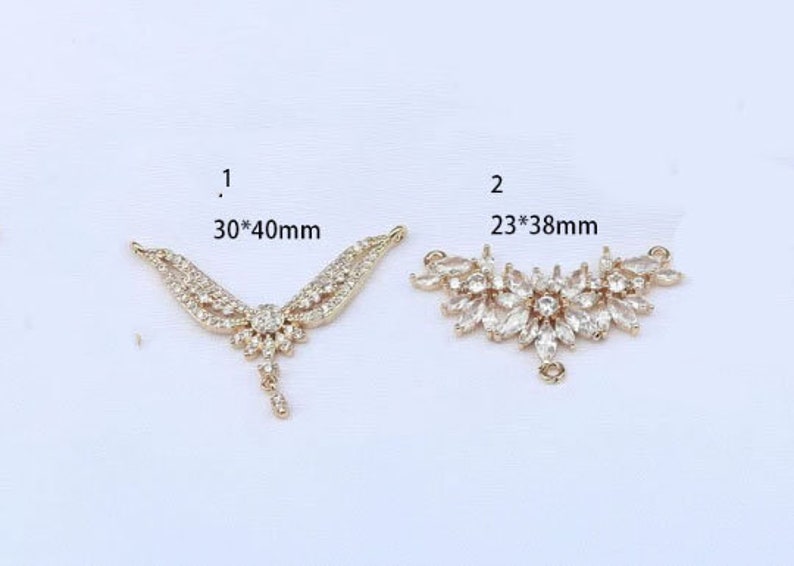 May include: Two gold-tone pendant connectors with clear crystal embellishments. The connector on the left measures 30mm by 40mm. The connector on the right measures 23mm by 38mm.
