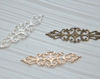 May include: Three decorative metal filigree pieces in silver, gold, and bronze. Each piece has a delicate, intricate design with a central diamond shape and swirling patterns.