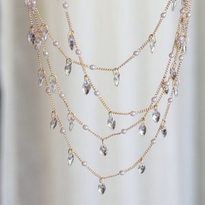 May include: A multi-layered gold chain necklace with delicate teardrop-shaped crystals hanging from each strand.