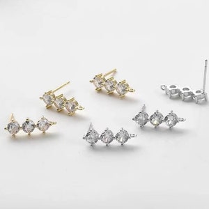 May include: Three pairs of earring findings with three clear cubic zirconia stones each. Two pairs are gold-toned and one pair is silver-toned.
