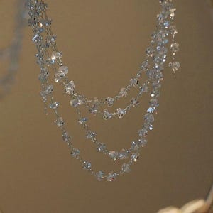 May include: A multi-strand necklace featuring delicate silver-toned chains adorned with numerous small, clear, faceted crystal beads. The beads are spaced evenly along the fine metal links, creating a layered, cascading effect of sparkling light.