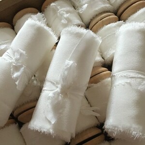 Op de afbeelding: Close-up van verschillende spoelen met wit gefranst lint, elk gewikkeld om een houten spoel.