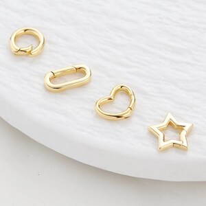 May include: Four gold-toned metal clasps in different shapes: a circle, an oval, a heart, and a star. The clasps are designed for attaching jewelry or other accessories.