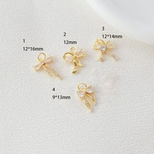 May include: Four gold-tone bow charms with clear rhinestones. The charms are different sizes, with measurements in millimeters.  1: 12*16mm, 2: 12mm, 3: 12*14mm, 4: 9*13mm.