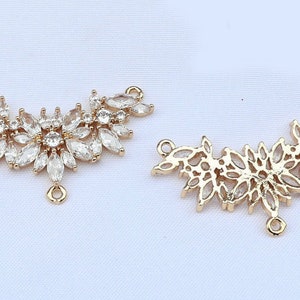 May include: Two gold-tone metal pendant charms with a leaf design. One charm is adorned with clear rhinestones, while the other is a simple outline.