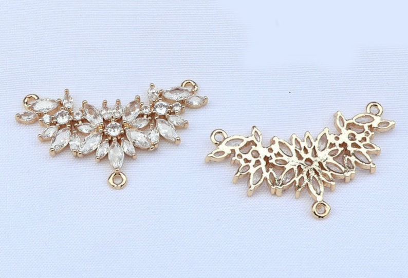 May include: Two gold-tone metal pendant charms with a leaf design. One charm is adorned with clear rhinestones, while the other is a simple outline.