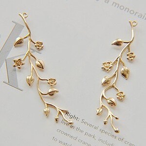 May include: Two gold-toned metal floral branch charms with delicate leaves and flowers. These charms are perfect for adding a touch of nature to jewellery projects.