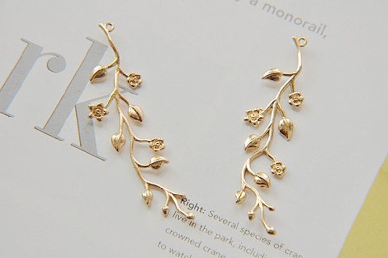May include: Two gold-toned metal floral branch charms with delicate leaves and flowers. These charms are perfect for adding a touch of nature to jewellery projects.