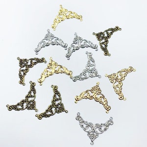 May include: Assortment of ornate metal corner embellishments in gold, silver, and bronze finishes. These decorative pieces feature intricate scrollwork and are perfect for adding a touch of vintage charm to craft projects.