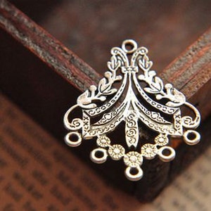 May include: A silver-toned metal jewelry connector featuring an intricate filigree design with symmetrical leaf-like patterns, a central vertical element, and five small circular loops along the bottom edge for attaching additional components.