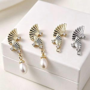 Peut inclure: Quatre composants de boucles d'oreilles en métal en forme d'éventails plissés avec de petits cristaux clairs. Deux pièces dorées présentent des perles blanches en forme de goutte, tandis que deux autres, une dorée et une argentée, ont des anneaux.