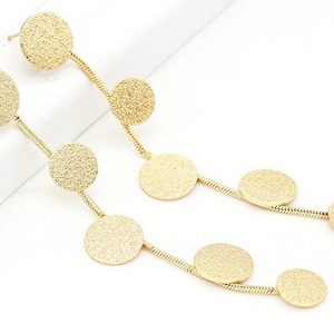 Può includere: Un paio di orecchini pendenti dorati con più dischi rotondi testurizzati collegati da una catena.