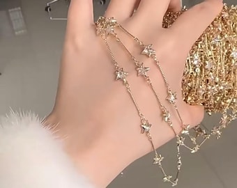 May include: Three gold chains with star-shaped charms. The chains are layered and the stars are evenly spaced.