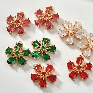 May include: Six gold flower charms with different colored gemstones. The charms are red, green, and clear. The charms are perfect for jewelry making or adding a touch of sparkle to any project.