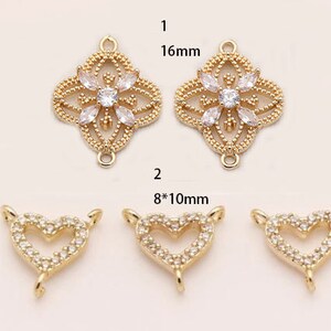 May include: Two gold-tone pendant charms with clear crystal accents. One charm is a 16 mm square with a floral design. The other charm is a heart shape measuring 8 mm by 10 mm.