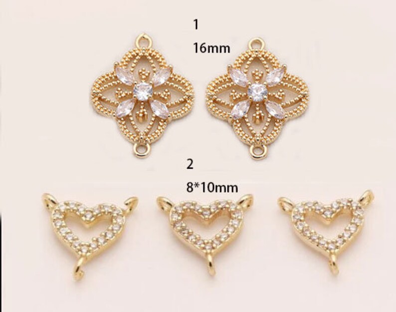 May include: Two gold-tone pendant charms with clear crystal accents. One charm is a 16 mm square with a floral design. The other charm is a heart shape measuring 8 mm by 10 mm.