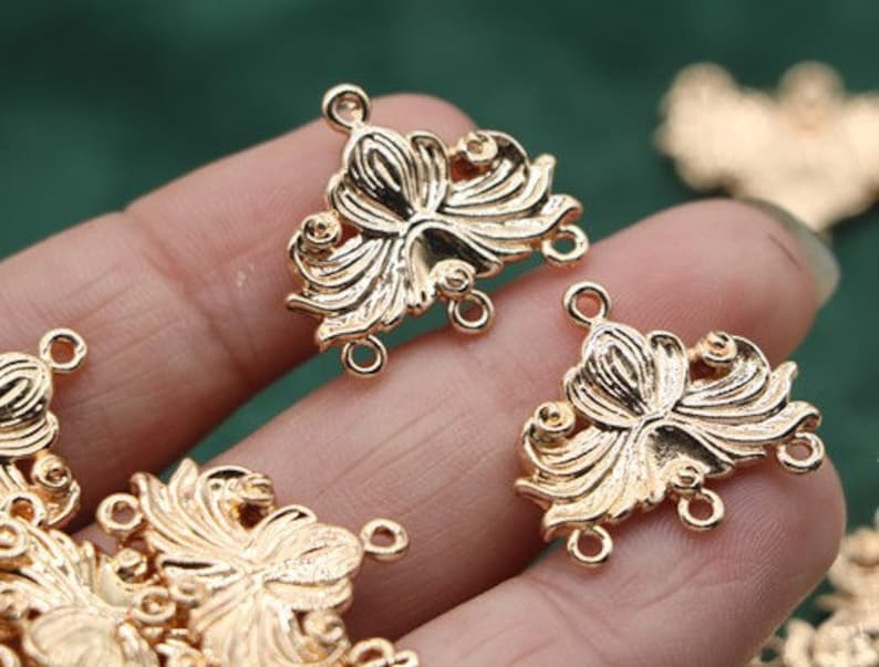 May include: Gold-tone metal connector charms with a floral design. Each charm has three loops for attaching jewelry pieces.