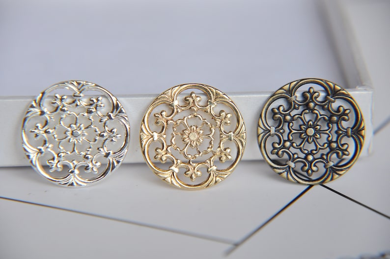 May include: Three decorative metal round ornaments with intricate floral designs. The ornaments are silver, gold, and bronze.