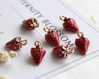 May include: Eight red strawberry charms with gold accents. The charms are on a white surface with the text "Eternity Blossom" in black.