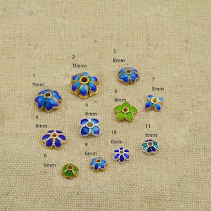 May include: Assortment of 11 enamel flower beads in various sizes, ranging from 6mm to 10mm. The beads are gold-toned with blue, green, and white enamel. The beads are numbered 1 through 11 with their corresponding size in millimetres.