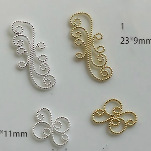 Puede incluir: Cuatro adornos decorativos de metal en plata y oro. Dos son alargados, miden 23mm x 9mm, y dos son más pequeños, miden 13mm x 11mm. Cada uno presenta un diseño en espiral, similar a una cuerda, ideal para la creación de joyas o manualidades.