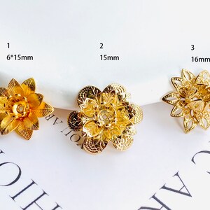 May include: Three gold-coloured metal flower-shaped embellishments with intricate designs. The embellishments are 6 x 15 mm, 15 mm, and 16 mm in size.