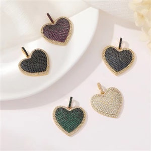 May include: Five gold heart-shaped pendants with different colored cubic zirconia stones. The pendants are on a white surface.