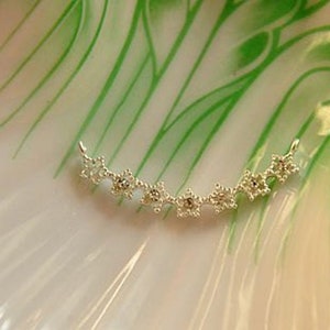 May include: A silver necklace with a delicate design of small, star-shaped charms. The necklace is curved into a crescent shape.