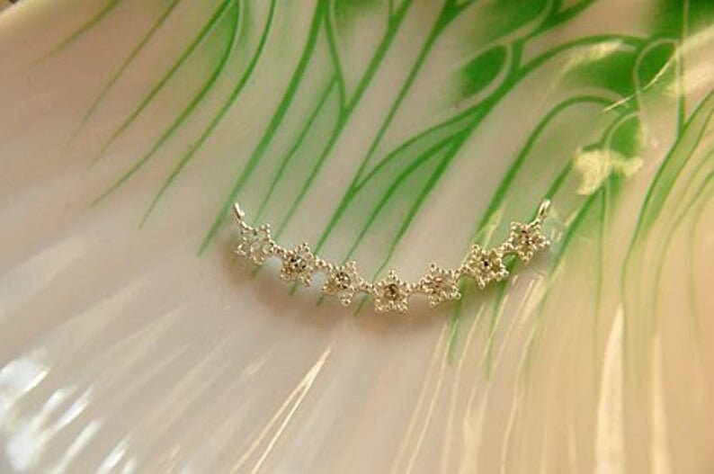 May include: A silver necklace with a delicate design of small, star-shaped charms. The necklace is curved into a crescent shape.
