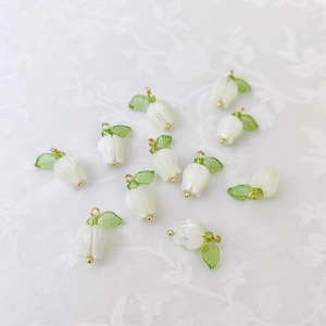 May include: A collection of white lily of the valley charms with green leaves and gold-colored accents. These delicate charms are ideal for jewelry making or other craft projects. The charms are small and detailed, perfect for adding a touch of nature to any design.