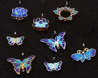 May include: Eight charm pendants with blue and gold enamel designs. The charms feature butterflies and lotus flowers.