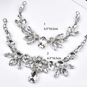 Op de afbeelding: Twee zilveren kettingen met kristallen strass, een is een kortere ketting met een traanvorm aan de onderkant, de andere is een langere ketting met een ronde vorm aan de onderkant. Beide kettingen zijn 4,3 inch bij 16,5 inch.